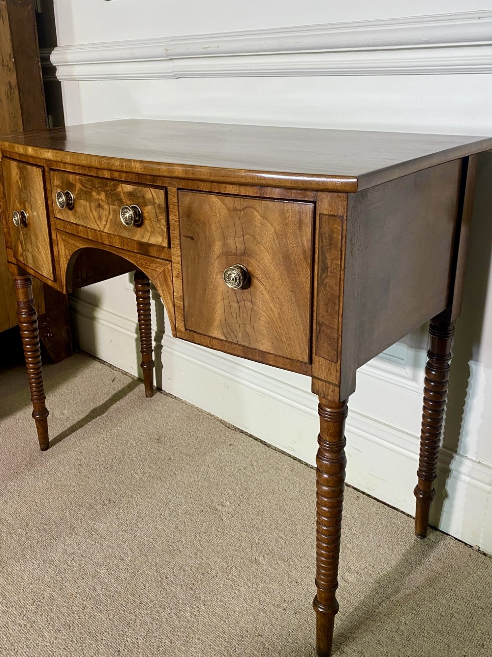 A George III bow-fronted mahogany dressing table featuring three drawers with round brass knobs, an arched central kneehole, and four turned legs. View III