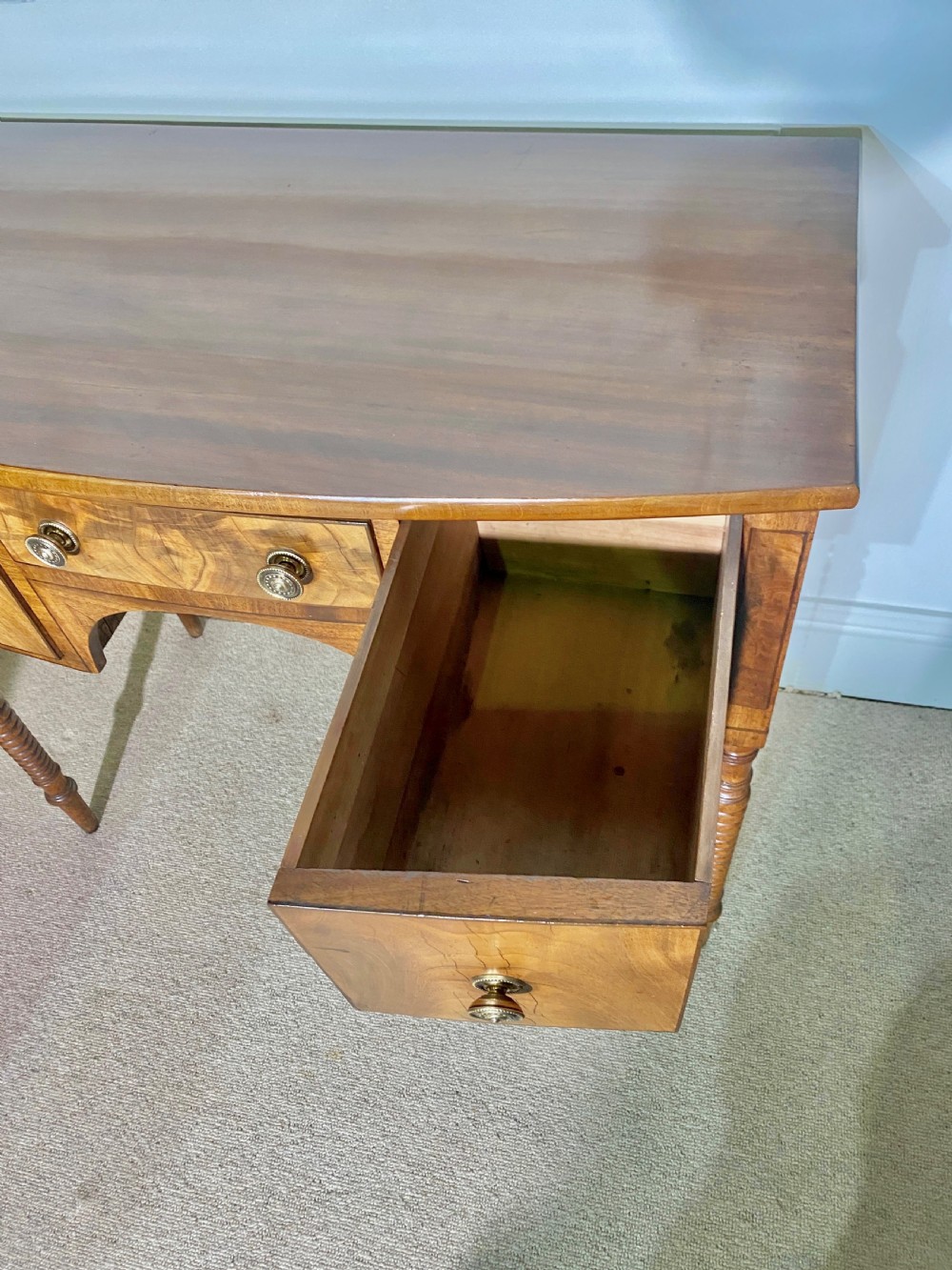 A George III bow-fronted mahogany dressing table featuring three drawers with round brass knobs, an arched central kneehole, and four turned legs. View IV