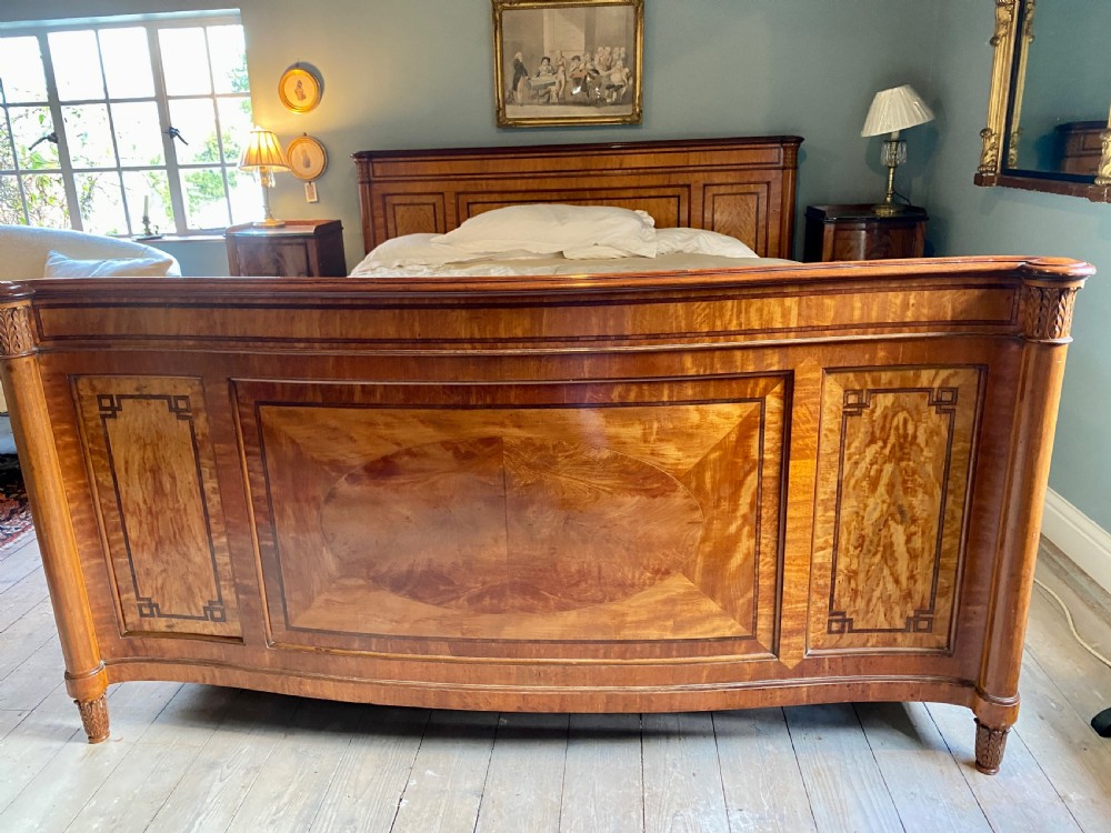 A nineteenth-century king-size satinwood bed frame featuring crossbanded panelling, an oval central veneer inlay on the footboard, and turned corner columns.