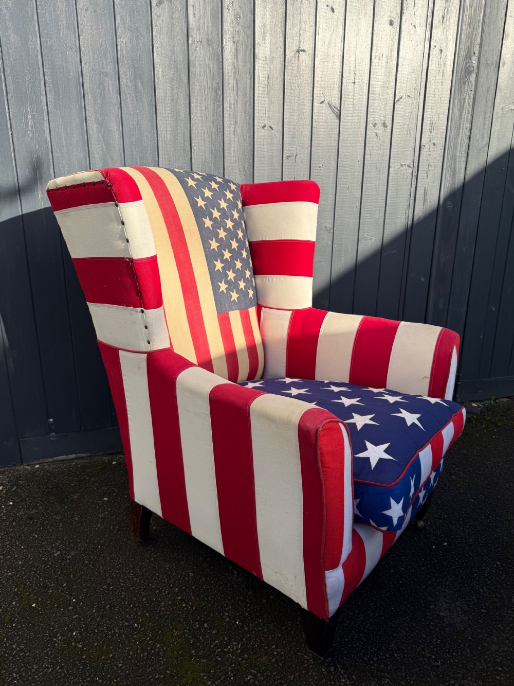 A Victorian style wingback armchair upholstered in an American stars and stripes flag pattern with turned dark wood front legs on brass castors. View II