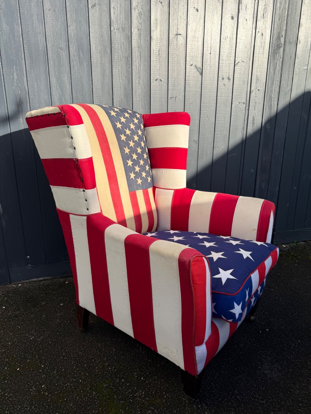 A Victorian style wingback armchair upholstered in an American stars and stripes flag pattern with turned dark wood front legs on brass castors. View IV