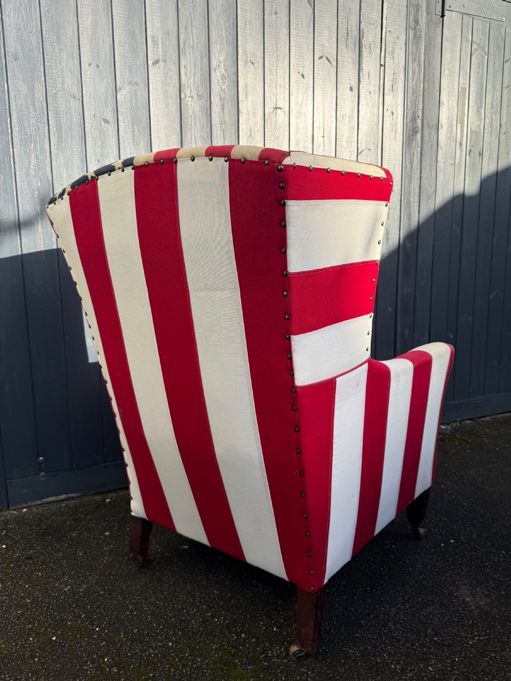 A Victorian style wingback armchair upholstered in an American stars and stripes flag pattern with turned dark wood front legs on brass castors. View V
