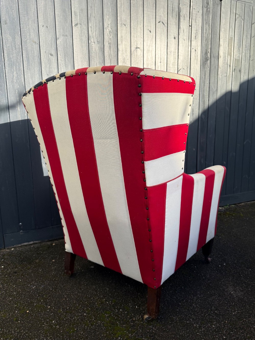 A Victorian style wingback armchair upholstered in an American stars and stripes flag pattern with turned dark wood front legs on brass castors. View VI