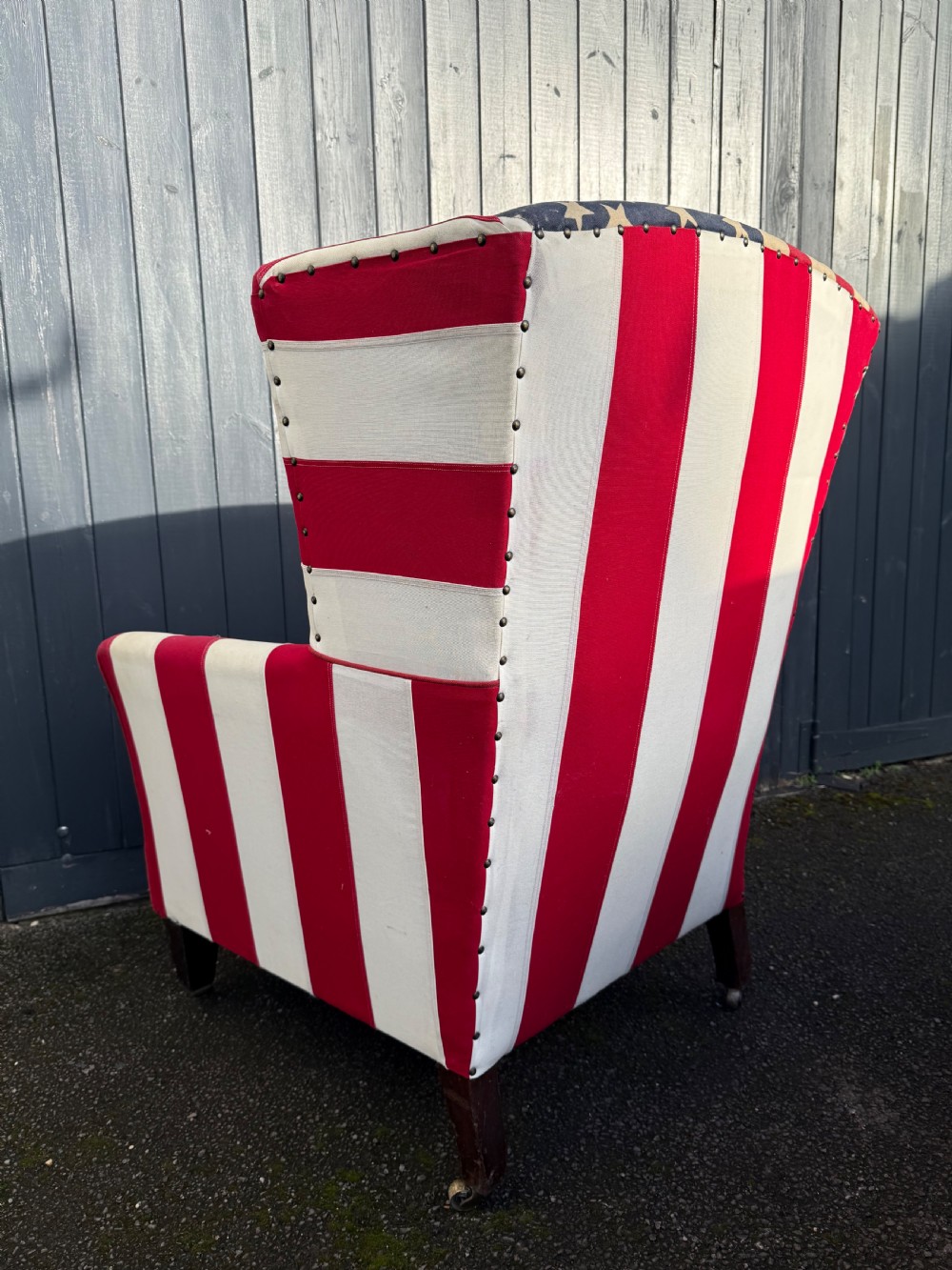 A Victorian style wingback armchair upholstered in an American stars and stripes flag pattern with turned dark wood front legs on brass castors. View VII
