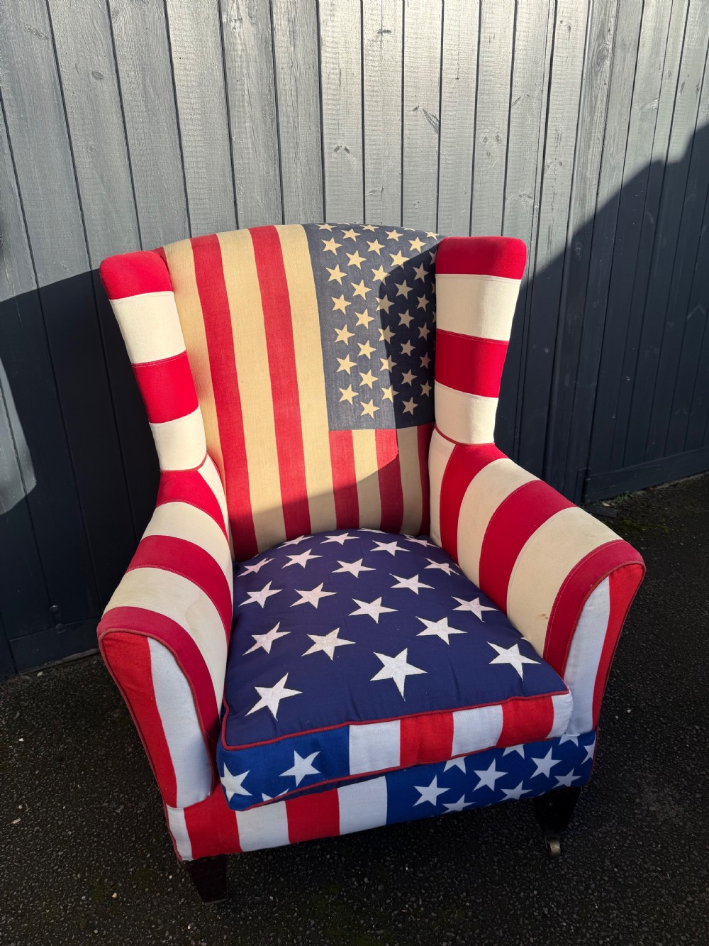 A Victorian style wingback armchair upholstered in an American stars and stripes flag pattern with turned dark wood front legs on brass castors. View VIII