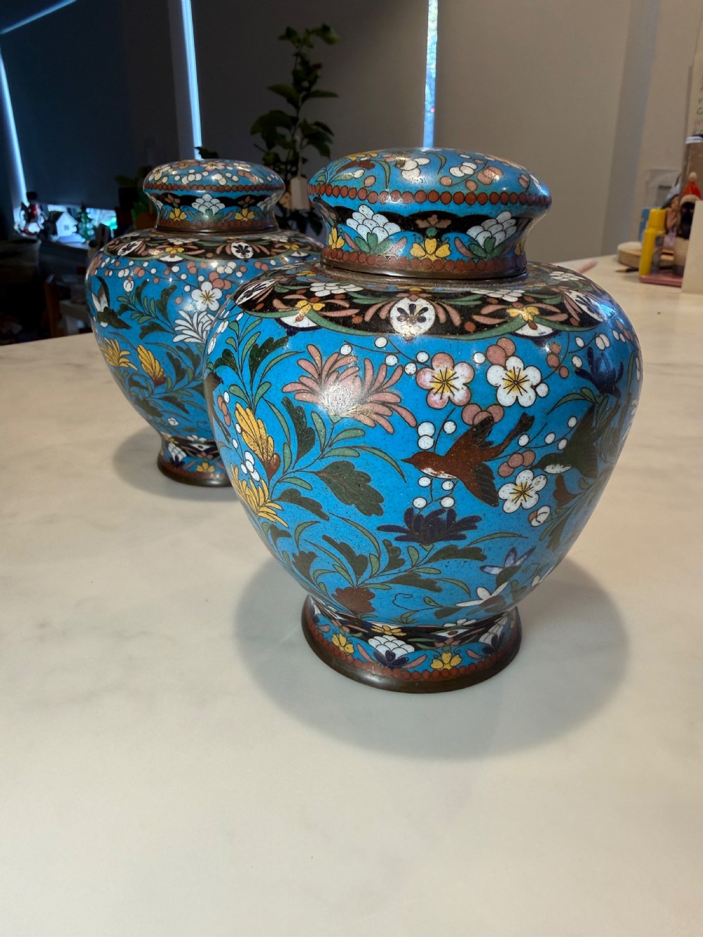 A pair of bulbous Japanese cloisonne ginger jars with lids, featuring intricate floral and bird motifs on a vibrant turquoise blue ground. View II