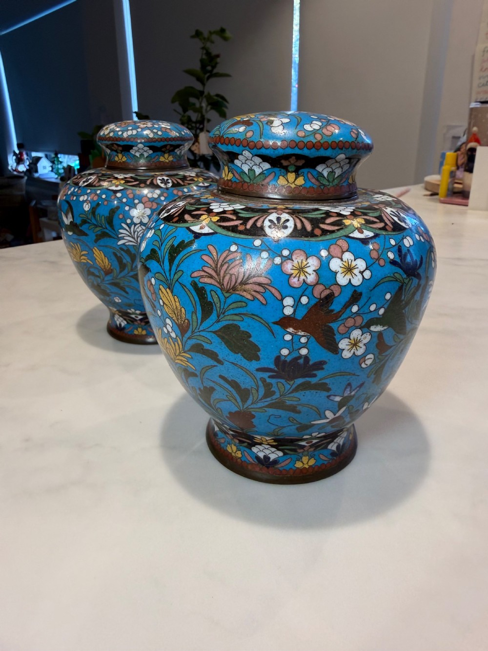 A pair of bulbous Japanese cloisonne ginger jars with lids, featuring intricate floral and bird motifs on a vibrant turquoise blue ground. View V