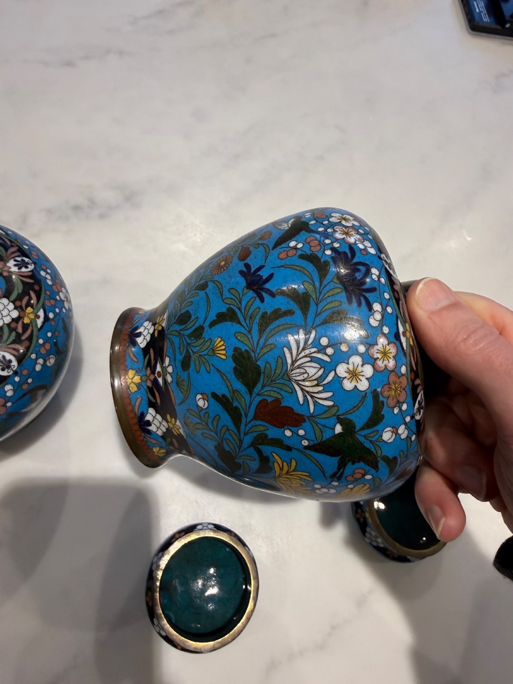 A pair of bulbous Japanese cloisonne ginger jars with lids, featuring intricate floral and bird motifs on a vibrant turquoise blue ground. View X