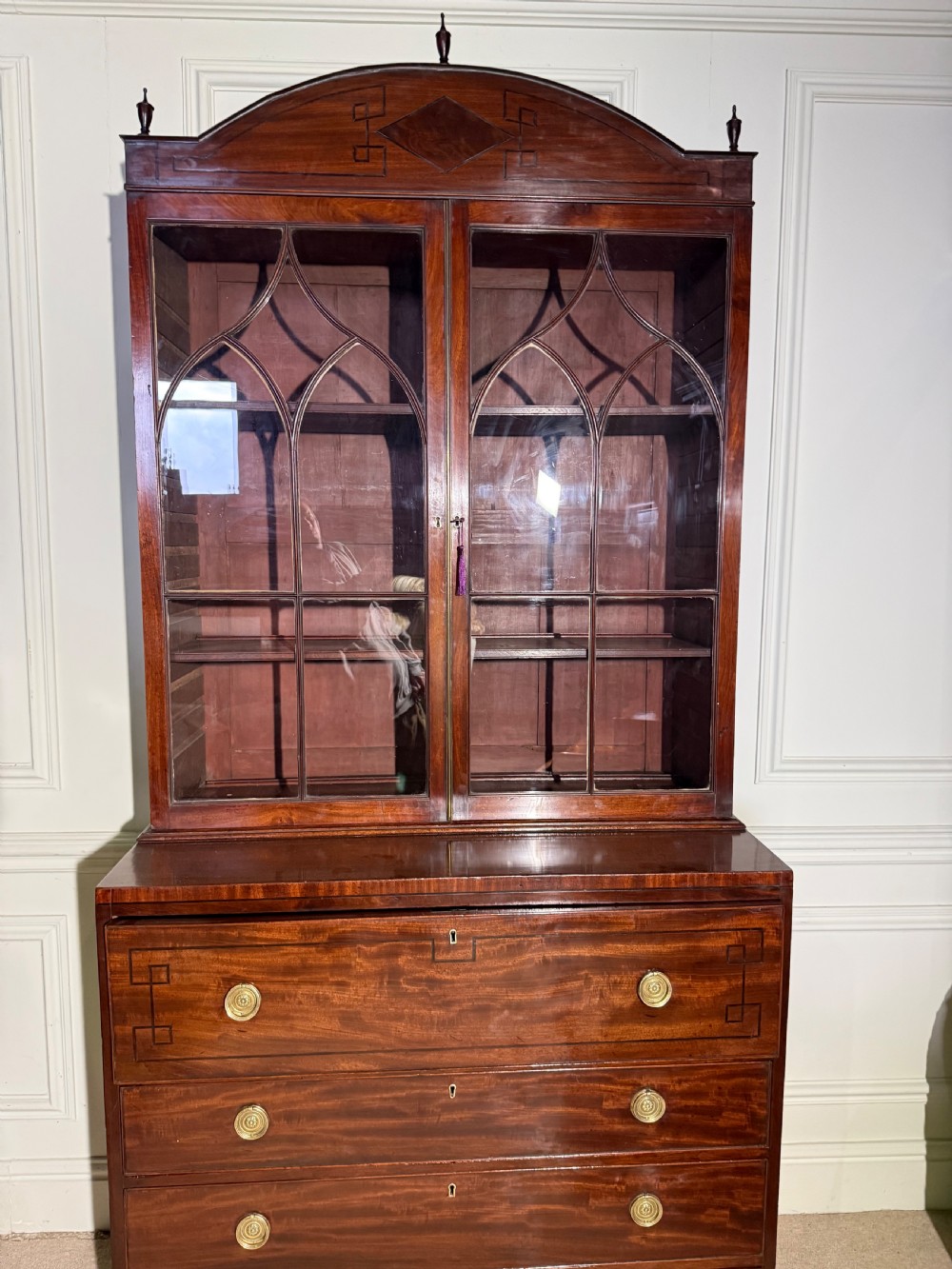 A tall Georgian mahogany secretaire bookcase featuring upper glazed doors with gothic arch bars, an arched pediment with finials, and a lower chest of drawers with brass ring handles. View VI