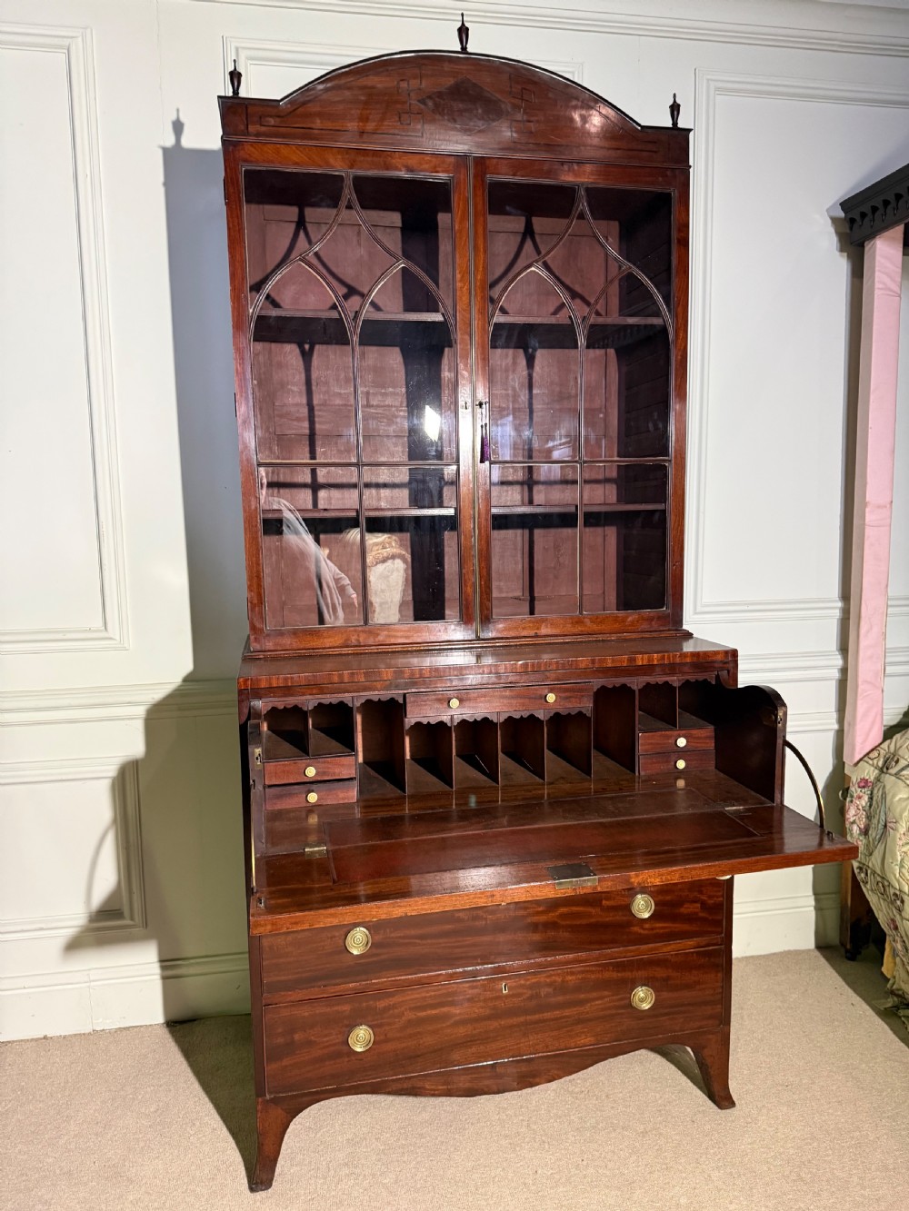 A tall Georgian mahogany secretaire bookcase featuring upper glazed doors with gothic arch bars, an arched pediment with finials, and a lower chest of drawers with brass ring handles. View X