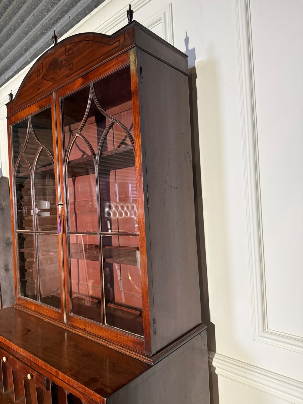 A tall Georgian mahogany secretaire bookcase featuring upper glazed doors with gothic arch bars, an arched pediment with finials, and a lower chest of drawers with brass ring handles. View XII