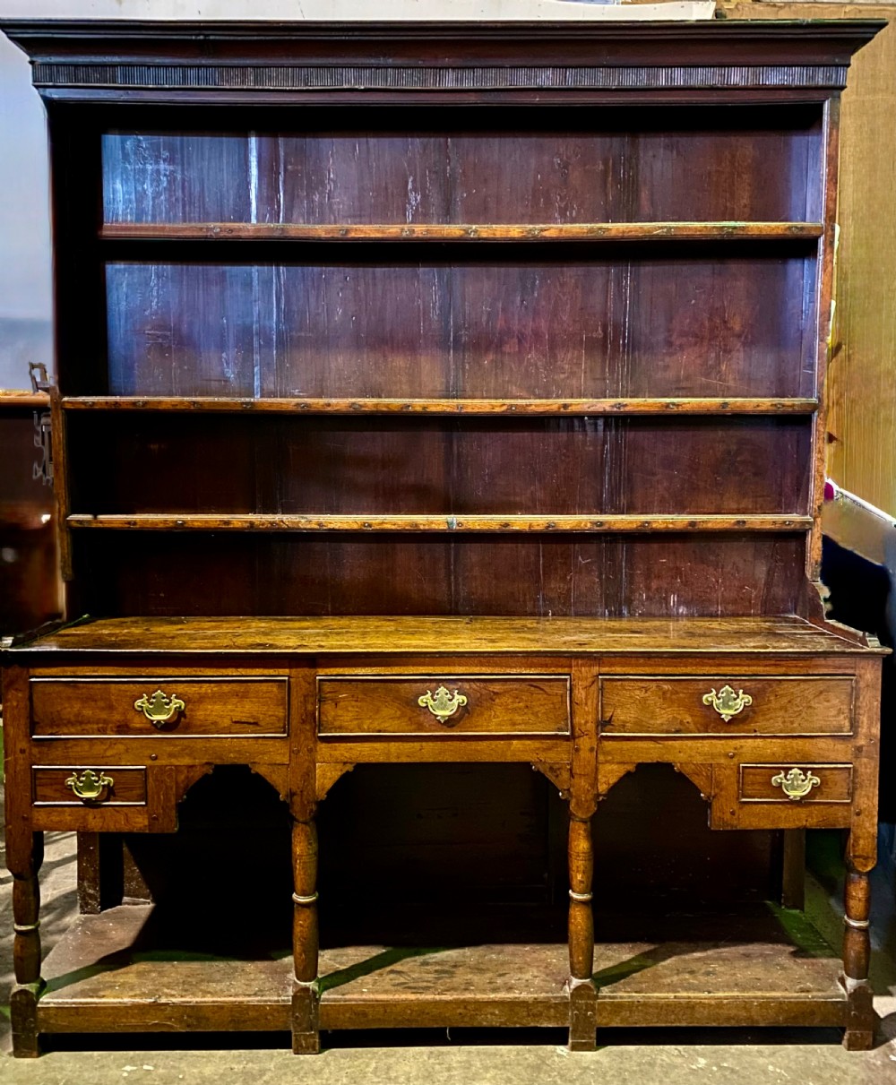 A Georgian oak dresser featuring a tall open plate rack top above five base drawers, turned legs, brass handles, and a lower pot board.