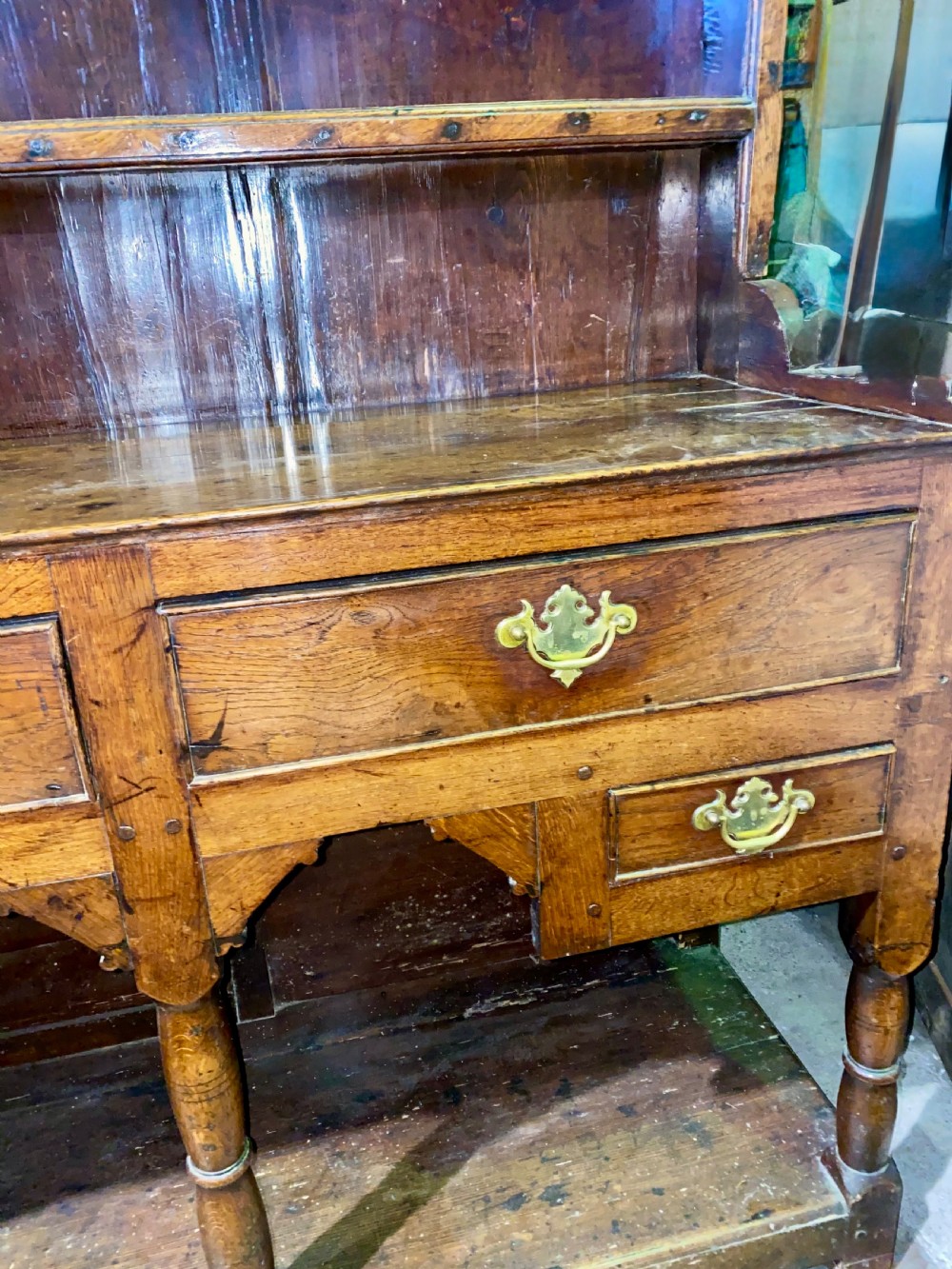 A Georgian oak dresser featuring a tall open plate rack top above five base drawers, turned legs, brass handles, and a lower pot board. View II