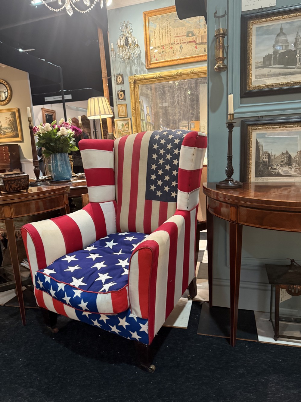 A Victorian style wingback armchair upholstered in an American stars and stripes flag pattern with turned dark wood front legs on brass castors.