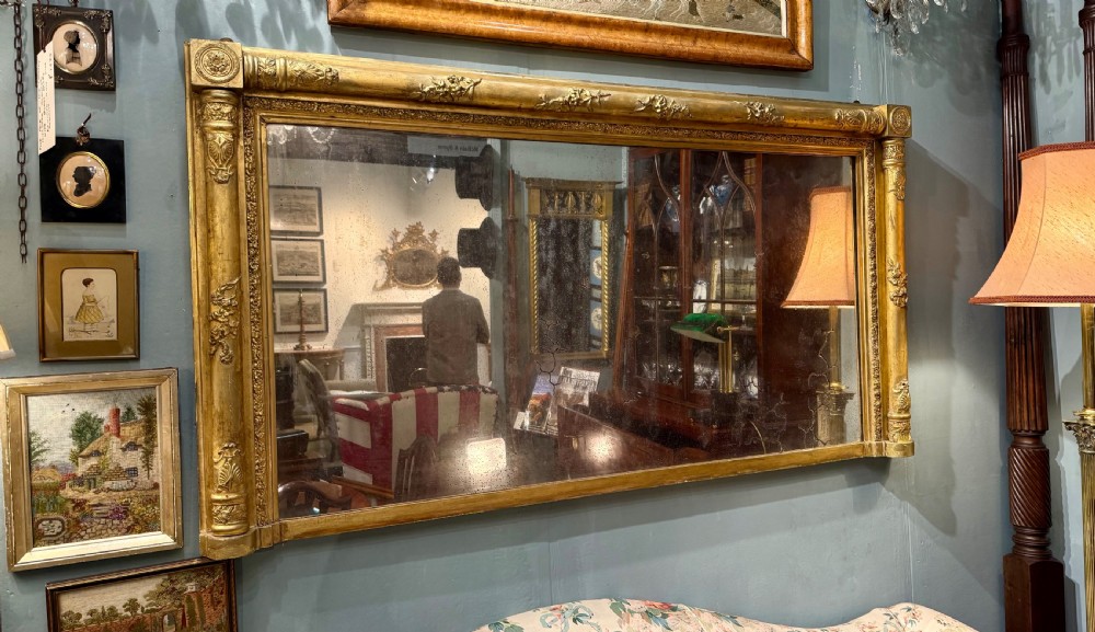A large rectangular Regency giltwood overmantel mirror featuring architectural fluted pilasters, corner rosettes, and floral moulding along the top frame.