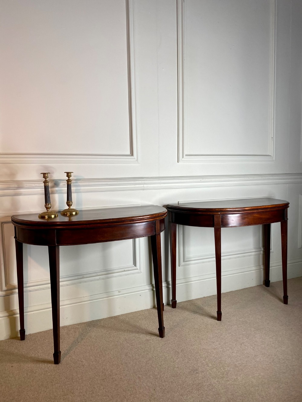 A pair of late eighteenth-century Georgian mahogany demilune card tables with fold-over tops and square tapered legs.