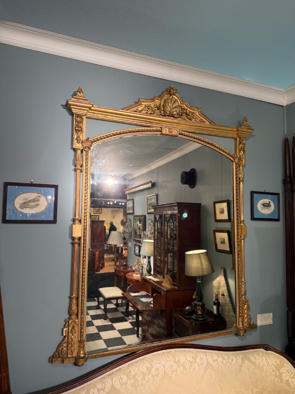 A 19th-century giltwood overmantel mirror featuring an arched top, detailed shell cresting, and carved side pilasters.