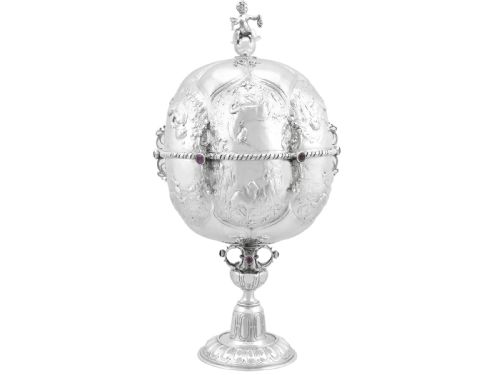 fig 1. An antique German sterling silver covered presentation cup featuring chased relief panels, set cabochon gemstones, and a putto finial.