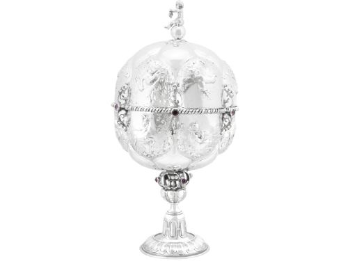 fig 3. An antique German sterling silver covered presentation cup featuring chased relief panels, set cabochon gemstones, and a putto finial.
