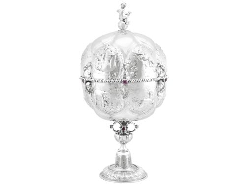 fig 2. An antique German sterling silver covered presentation cup featuring chased relief panels, set cabochon gemstones, and a putto finial.