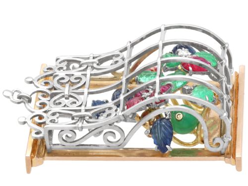 fig 5. An 18ct gold window-framed brooch featuring carved emerald, ruby, and sapphire floral elements behind a silver-coloured metal grate.
