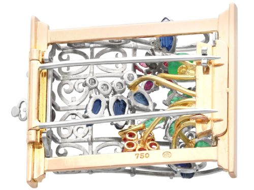 fig 6. An 18ct gold window-framed brooch featuring carved emerald, ruby, and sapphire floral elements behind a silver-coloured metal grate.