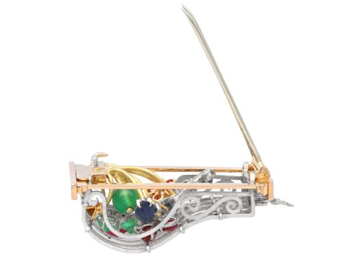 fig 7. An 18ct gold window-framed brooch featuring carved emerald, ruby, and sapphire floral elements behind a silver-coloured metal grate.