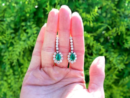 fig 1. A pair of 18ct white gold drop earrings featuring pear-cut green emeralds surrounded by round diamond halos suspended from vertical diamond bars.