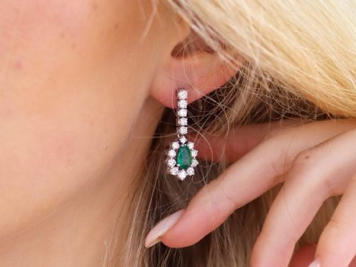 fig 2. A pair of 18ct white gold drop earrings featuring pear-cut green emeralds surrounded by round diamond halos suspended from vertical diamond bars.
