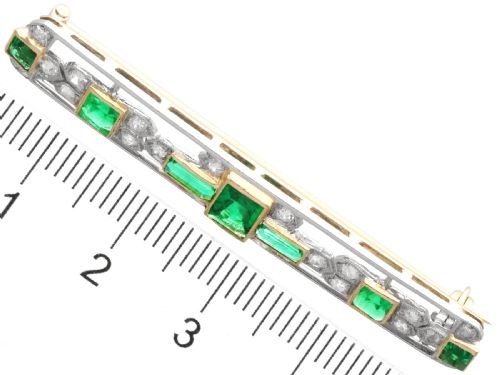 fig 6. An elongated 9ct yellow gold bar brooch featuring a central step-cut emerald flanked by geometric diamond-set panels and smaller emerald accents.