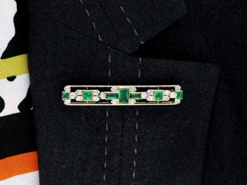 fig 8. An elongated 9ct yellow gold bar brooch featuring a central step-cut emerald flanked by geometric diamond-set panels and smaller emerald accents.