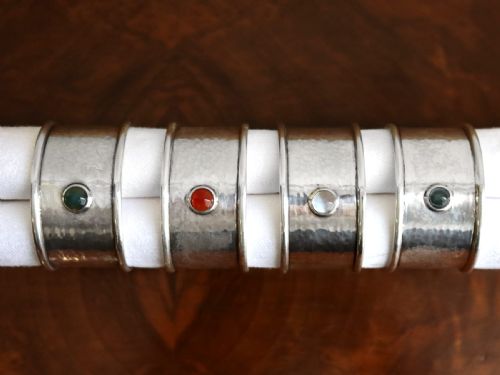 fig 1. A set of four circular sterling silver napkin rings with planished hand-hammered textures, each inset with a distinct coloured cabochon stone.
