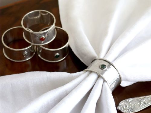 fig 2. A set of four circular sterling silver napkin rings with planished hand-hammered textures, each inset with a distinct coloured cabochon stone.
