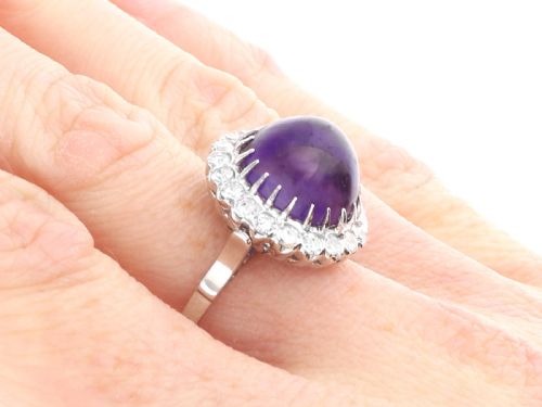 fig 7. An antique platinum dress ring set with a large central purple cabochon amethyst surrounded by a halo of round diamonds.