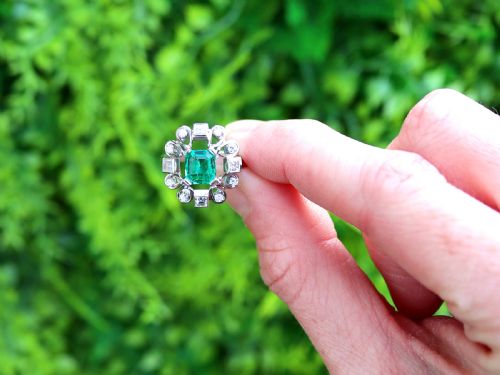 fig 1. An Art Deco 18ct white gold ring featuring a central octagonal green emerald surrounded by geometric diamond-set loop mounts.