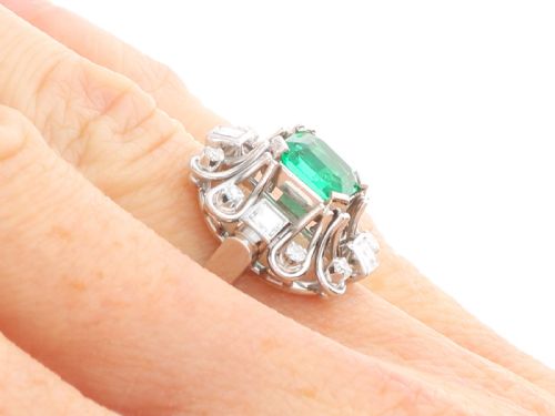 fig 6. An Art Deco 18ct white gold ring featuring a central octagonal green emerald surrounded by geometric diamond-set loop mounts.