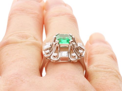 fig 7. An Art Deco 18ct white gold ring featuring a central octagonal green emerald surrounded by geometric diamond-set loop mounts.