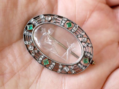 fig 2. An oval Victorian brooch featuring a reverse-carved rock crystal intaglio depicting Cupid and Psyche, bordered by rose-cut diamonds and square-cut emeralds set in gold and silver.