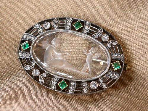 fig 3. An oval Victorian brooch featuring a reverse-carved rock crystal intaglio depicting Cupid and Psyche, bordered by rose-cut diamonds and square-cut emeralds set in gold and silver.