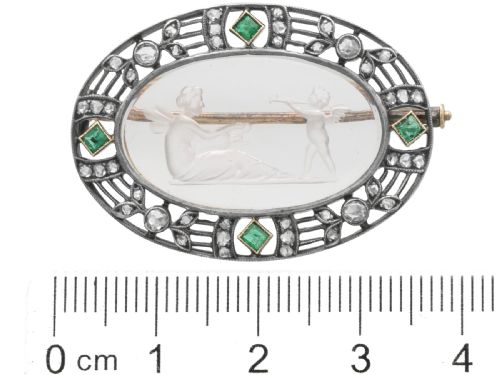 fig 7. An oval Victorian brooch featuring a reverse-carved rock crystal intaglio depicting Cupid and Psyche, bordered by rose-cut diamonds and square-cut emeralds set in gold and silver.