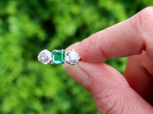fig 1. An Art Deco platinum trilogy ring featuring a central emerald-cut green emerald flanked by two round diamonds.