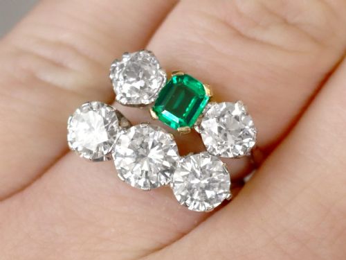 fig 2. An Art Deco platinum trilogy ring featuring a central emerald-cut green emerald flanked by two round diamonds.