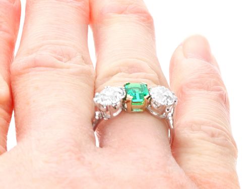 fig 8. An Art Deco platinum trilogy ring featuring a central emerald-cut green emerald flanked by two round diamonds.