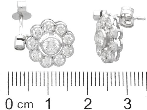 fig 6. A pair of Art Deco 18ct white gold drop earrings featuring a circular diamond cluster motif suspended from a single bezel-set diamond surmount.