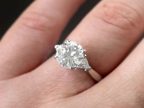 fig 4. A vintage platinum ring featuring a large round brilliant central diamond flanked by two triangular side diamonds on a smooth metal band.