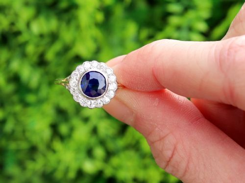fig 1. An antique 18ct yellow gold ring featuring a central round blue sapphire encircled by a halo of bright diamonds set within a scalloped millegrain bezel.