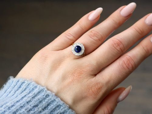 fig 2. An antique 18ct yellow gold ring featuring a central round blue sapphire encircled by a halo of bright diamonds set within a scalloped millegrain bezel.