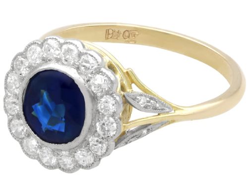 fig 4. An antique 18ct yellow gold ring featuring a central round blue sapphire encircled by a halo of bright diamonds set within a scalloped millegrain bezel.