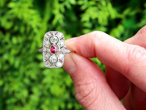 fig 1. An Art Deco 14ct yellow gold dress ring featuring a central oval red ruby set within a rectangular pierced openwork plaque adorned with round diamonds and millegrain edging.