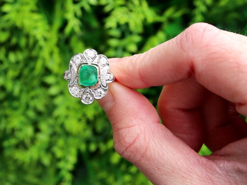 fig 1. An Art Deco dress ring featuring a central cushion-cut green emerald surrounded by a geometric pierced diamond halo set in white metal on an 18ct yellow gold band.